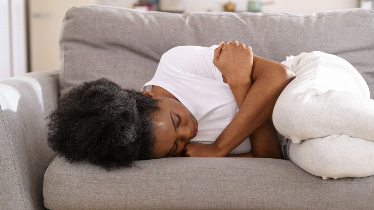 Regelschmerzen lindern Tipps und Tricks, Frau mit Unterleibschmerzen auf dem Sofa