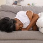 Regelschmerzen lindern Tipps und Tricks, Frau mit Unterleibschmerzen auf dem Sofa