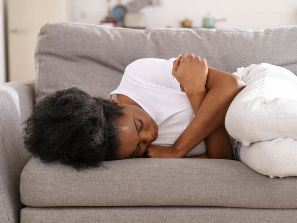 Regelschmerzen lindern Tipps und Tricks, Frau mit Unterleibschmerzen auf dem Sofa