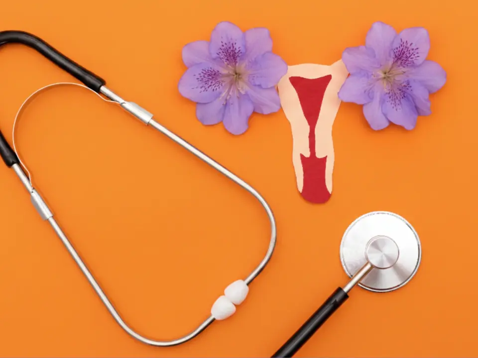 Ilustración del útero femenino con flujo menstrual junto a un estetoscopio sobre fondo naranja, representando la salud ginecológica.