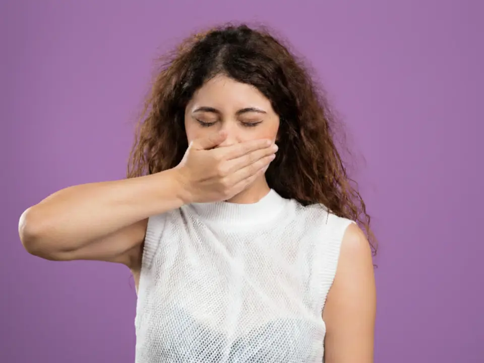 Woman with closed eyes covering her mouth with her hand against a purple background