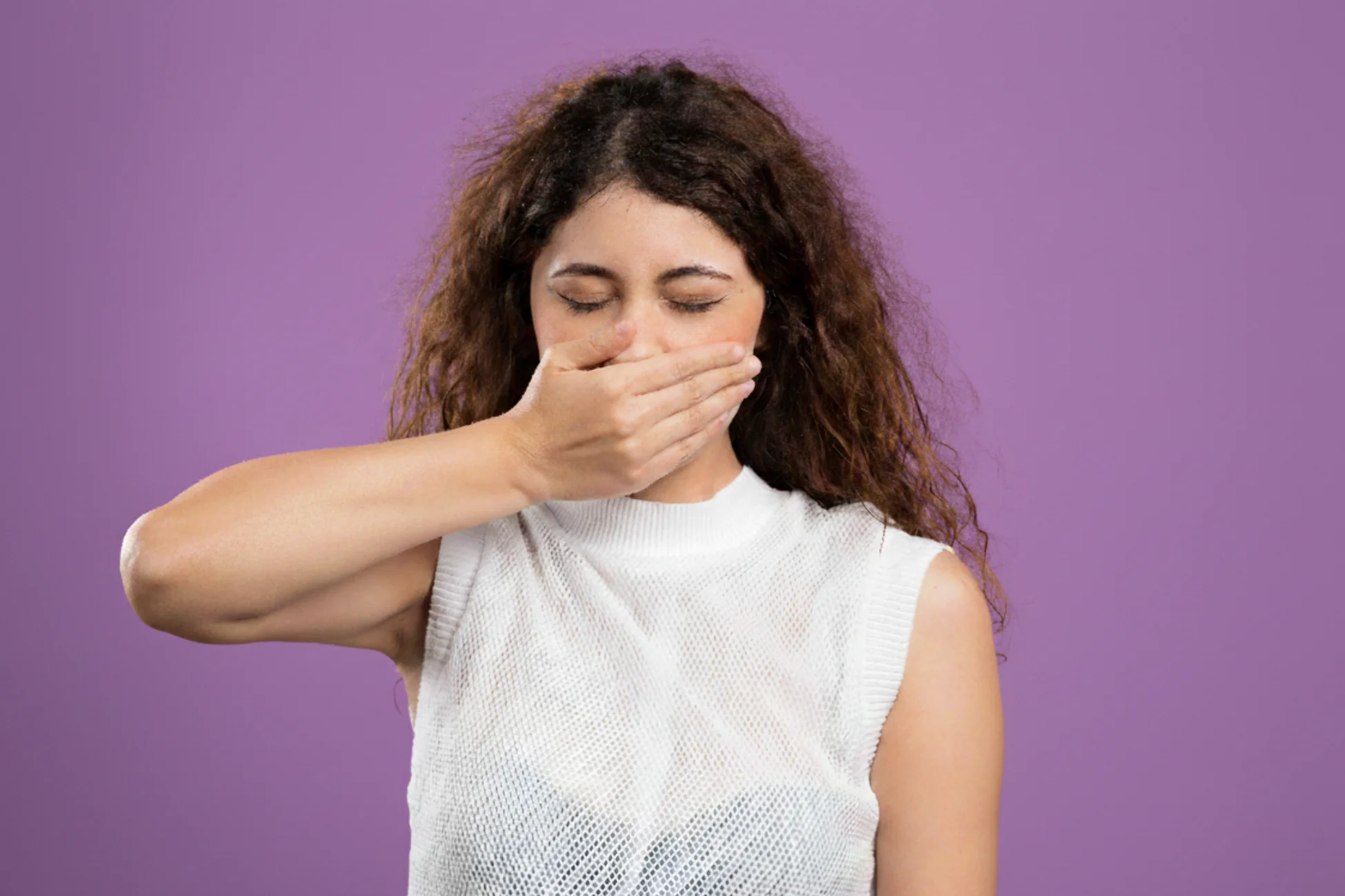 Woman with closed eyes covering her mouth with her hand against a purple background