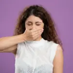 Femme aux yeux fermés couvrant sa bouche avec la main sur fond violet