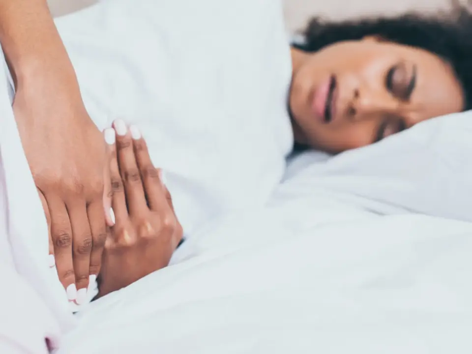 Woman lying in bed holding her lower abdomen due to menstrual cramps during her period.