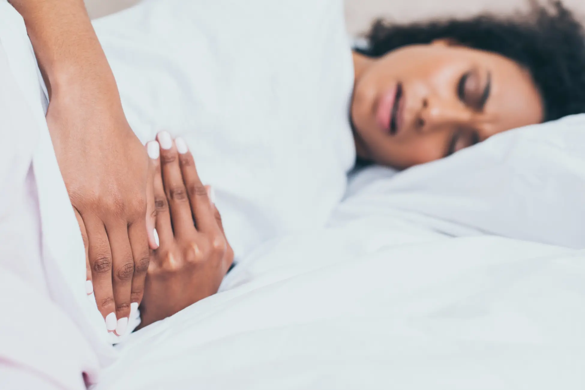 Woman lying in bed holding her lower abdomen due to menstrual cramps during her period.