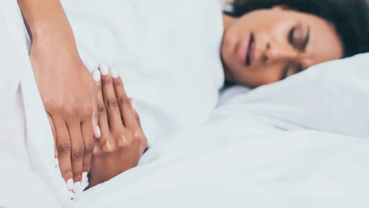 Femme allongée dans son lit tenant son bas-ventre à cause de douleurs menstruelles.