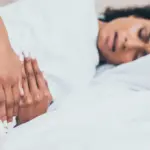 Femme allongée dans son lit tenant son bas-ventre à cause de douleurs menstruelles.