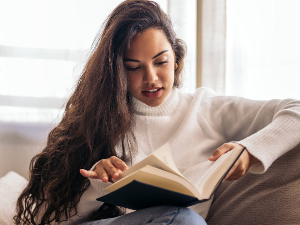 Mujer joven leyendo un libro de bienestar femenino en casa