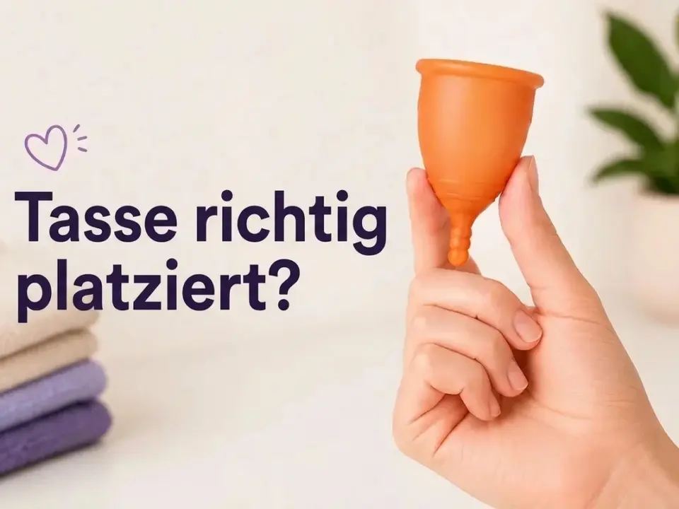 Eine Hand hält eine orange Menstruationstasse vor hellem Hintergrund mit lila Text "¿Copa bien colocada?".