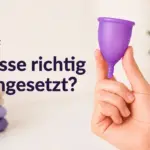 Hand hält lila Menstruationstasse; dazu spanischer Text „Copa bien colocada?“ und Herzsymbol.