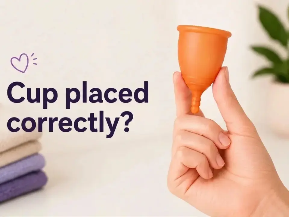 An orange menstrual cup is held by a hand, alongside the question "¿Copa bien colocada?" and stacked towels.