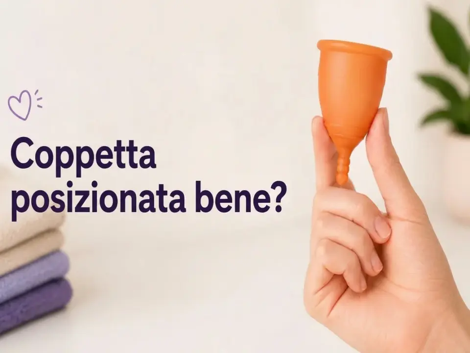Mano che mostra una coppetta mestruale arancione con il testo "¿Copa bien colocada?" e asciugamani sullo sfondo.