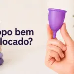 Mão segura uma copa menstrual roxa com a pergunta ¿Copa bien colocada?.
